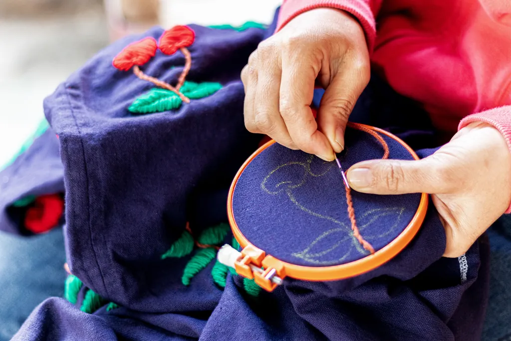 Mains brodant un motif au fil orange sur un tambour, sur un tissu bleu