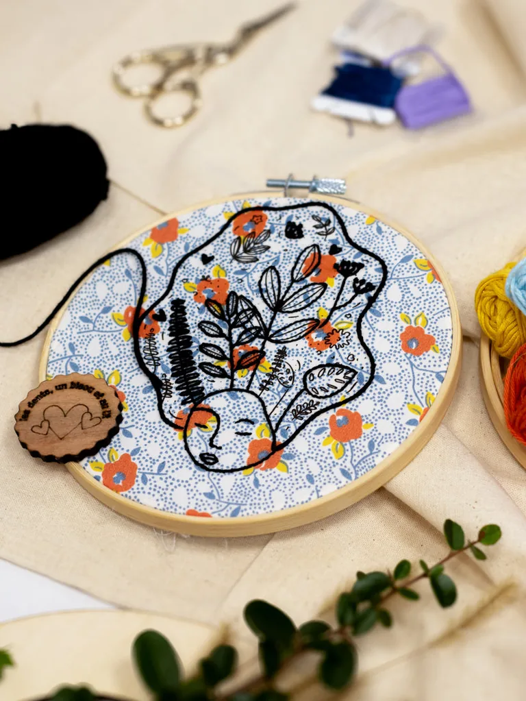 Broderie d’un visage de femme aux cheveux fleuris sur tissu liberty, dans un tambour