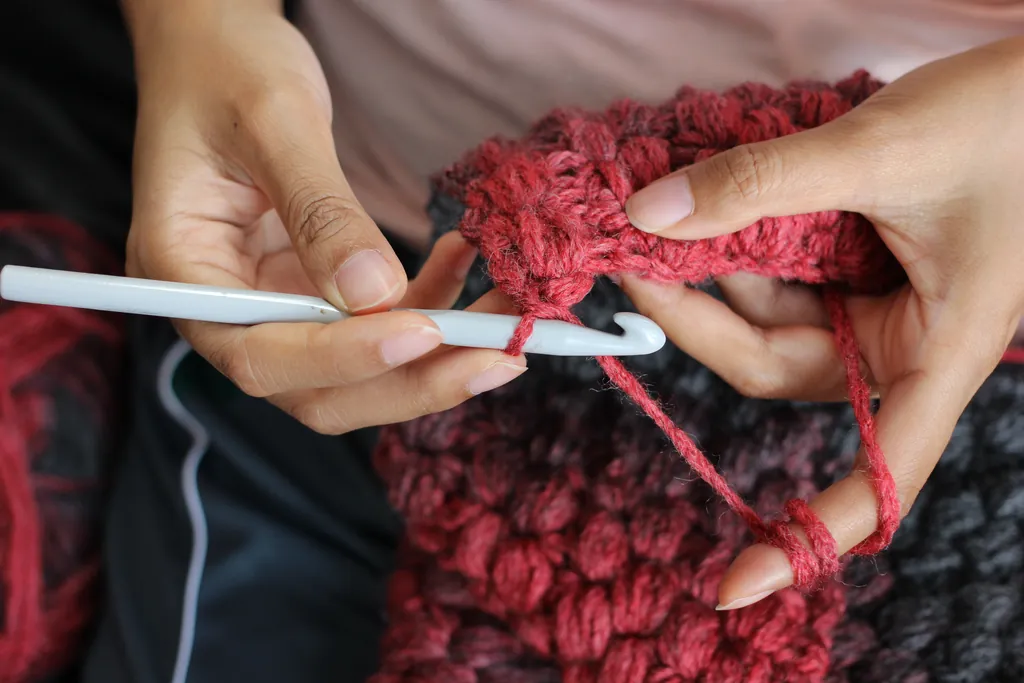 Mains maniant un crochet blanc sur un ouvrage en laine rouge