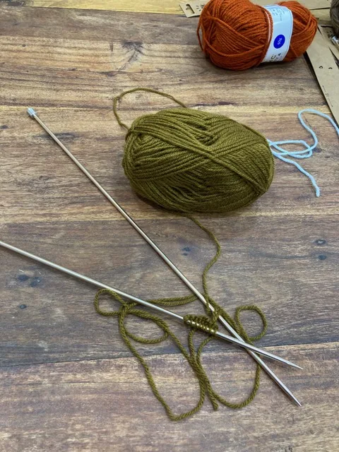 Aiguilles à tricoter et pelote de laine vert olive sur une table en bois