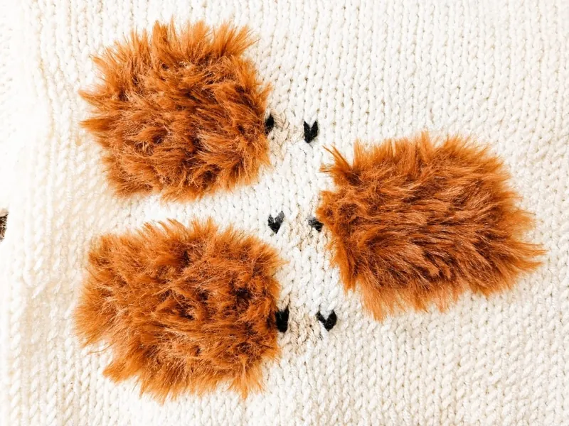 Des pompons en fausse fourrure sur un tricot écru