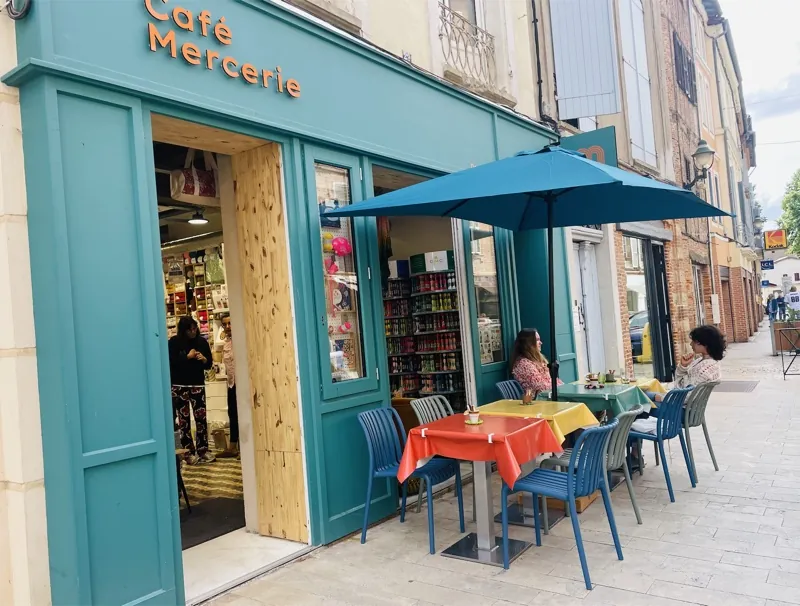 La terrasse de Moha devant la façade bleu canard : tables colorées et chaises sous le parasol